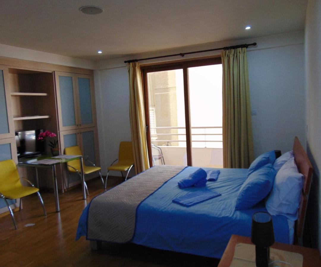 a bedroom with a blue bed and a balcony at Ithaki Phinikoudes Apartment No. 107 in Larnaka