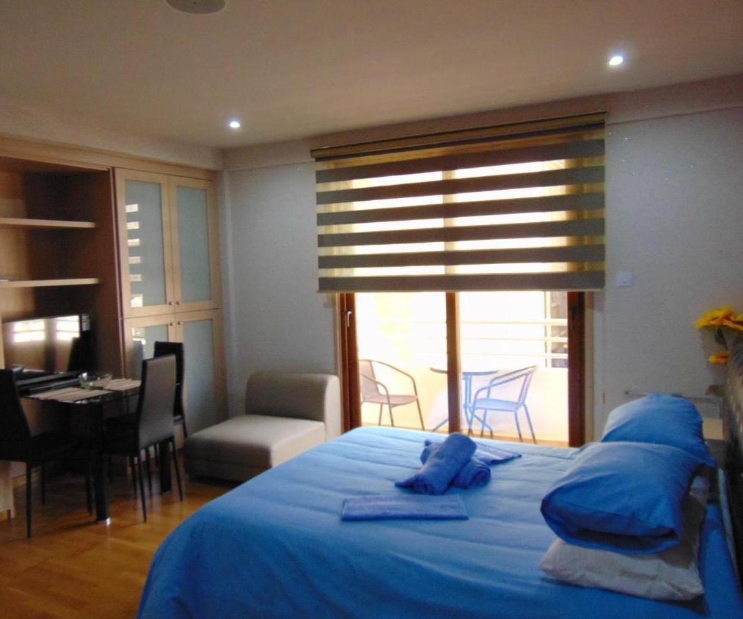 a bedroom with a bed with blue pillows and a table at Ithaki Phinikoudes Apartment No. 207 in Larnaka