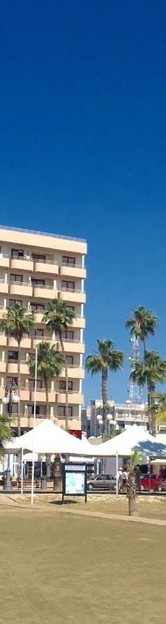 a large hotel building with palm trees and umbrellas at Ithaki Phinikoudes Apartments No. 106 in Larnaka