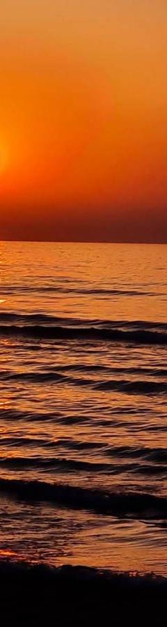 an orange sunset over the ocean with a beach at Ithaki Phinikoudes Apartment No. 102 in Larnaka